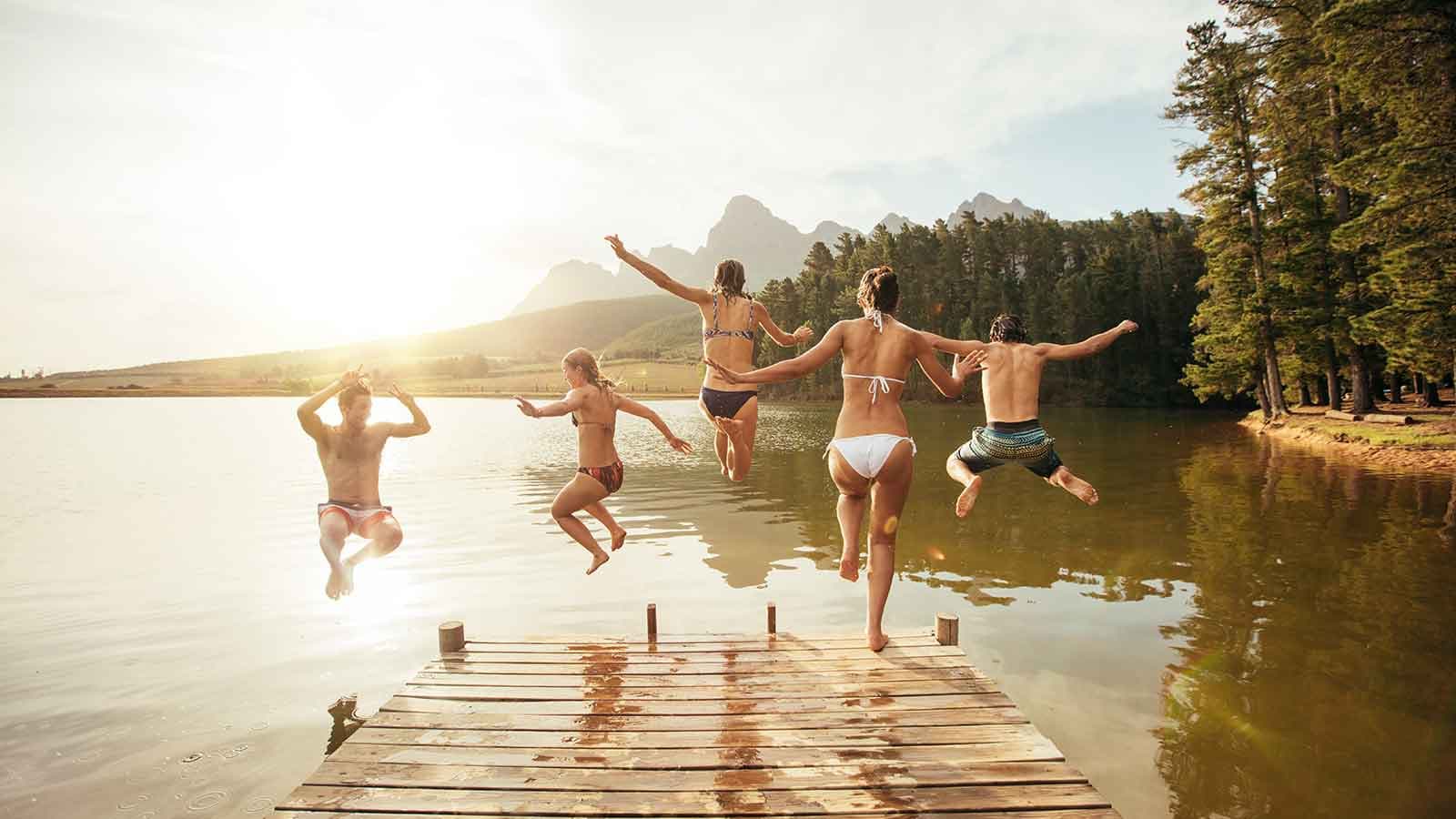 Adults wearing swimwear jumping off jetty into lake