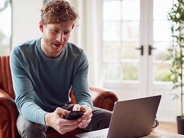 Man sitting in living room with laptop and smartphone