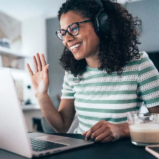 Woman wearing headphone and waving at video call on laptop