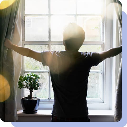 Man opening curtains with sunlight shining