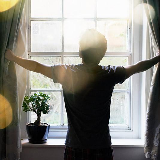 A man drawing back the curtains to reveal bright sunshine