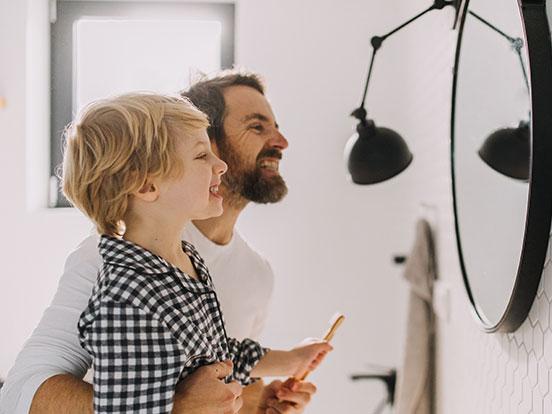 Father and son brushing together at bathroom mirror