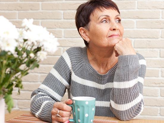 Woman sat at a table with a mug and her head resting in her hand