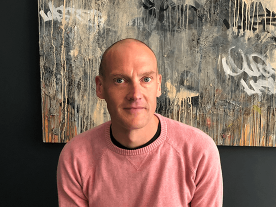 White man in pink jumper sat in front of abstract art