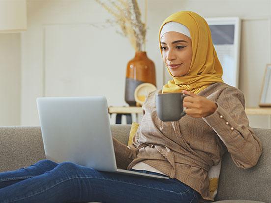 Woman sitting on the sofa with a laptop on her lap, holding a cup