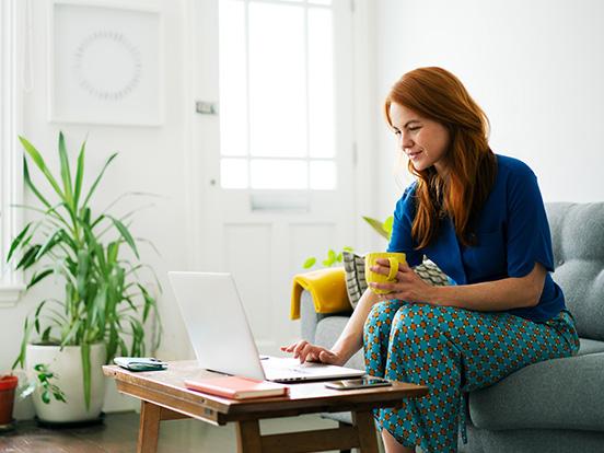 Woman using a laptop whilst sitting on a sofa at home