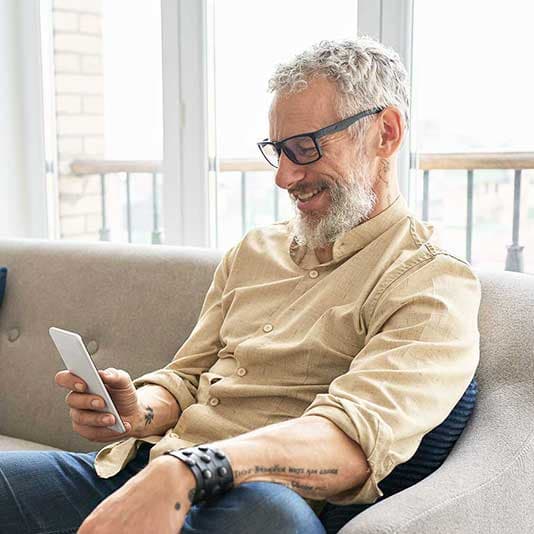 Relaxed man wearing glasses using phone on sofa