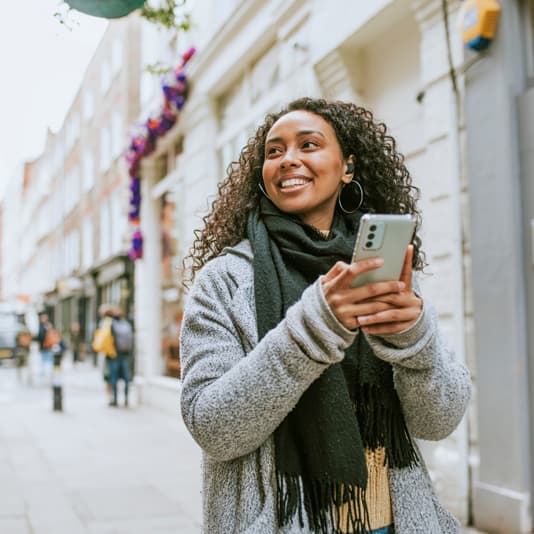 Woman walking down street smiling holding phone