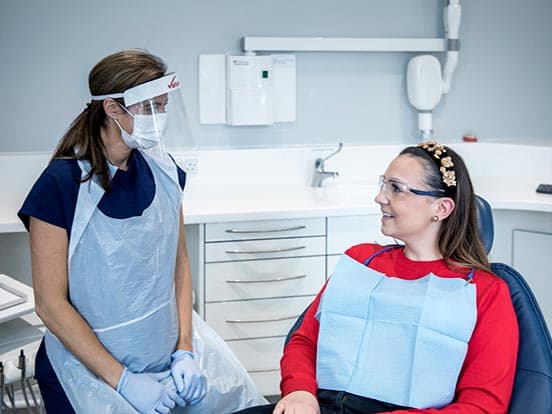 Dentist wearing PPE talking to a patient in a treatment room