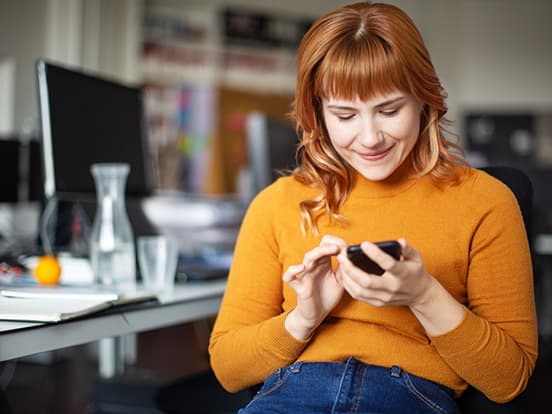 Woman using a smart phone sat at desk in office