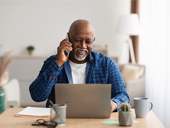 Man on a phone call in front of his laptop at home