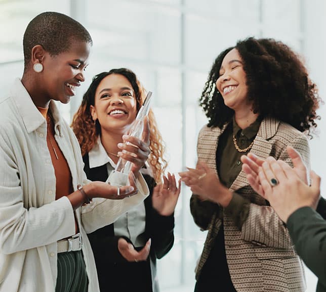 Three people celebrating as one holds an award. They are smiling and applauding, standing in a bright, modern space.